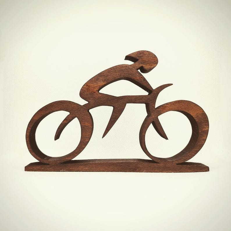 Peut inclure: Sculpture en bois brun fonc&eacute; repr&eacute;sentant un cycliste sur un v&eacute;lo. Le design est minimaliste, avec le cycliste en position de conduite. Les roues du v&eacute;lo sont circulaires, et la sculpture est mont&eacute;e sur une base.