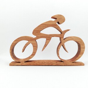 Peut inclure: Sculpture en bois repr&eacute;sentant un cycliste sur un v&eacute;lo. La sculpture est faite de bois brun clair et repr&eacute;sente un cycliste portant un casque, pench&eacute; sur le guidon. Le v&eacute;lo a de grandes roues stylis&eacute;es et est mont&eacute; sur une base rectangulaire.