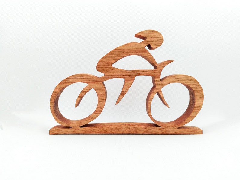 Peut inclure: Sculpture en bois repr&eacute;sentant un cycliste sur un v&eacute;lo. La sculpture est faite de bois brun clair et repr&eacute;sente un cycliste portant un casque, pench&eacute; sur le guidon. Le v&eacute;lo a de grandes roues stylis&eacute;es et est mont&eacute; sur une base rectangulaire.