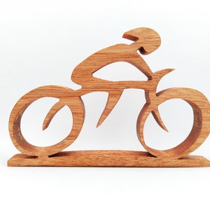Peut inclure: Sculpture en bois repr&eacute;sentant un cycliste sur un v&eacute;lo. La sculpture est faite de bois brun clair et repr&eacute;sente un cycliste portant un casque, pench&eacute; sur le guidon. Les roues et le cadre du v&eacute;lo sont &eacute;galement en bois.
