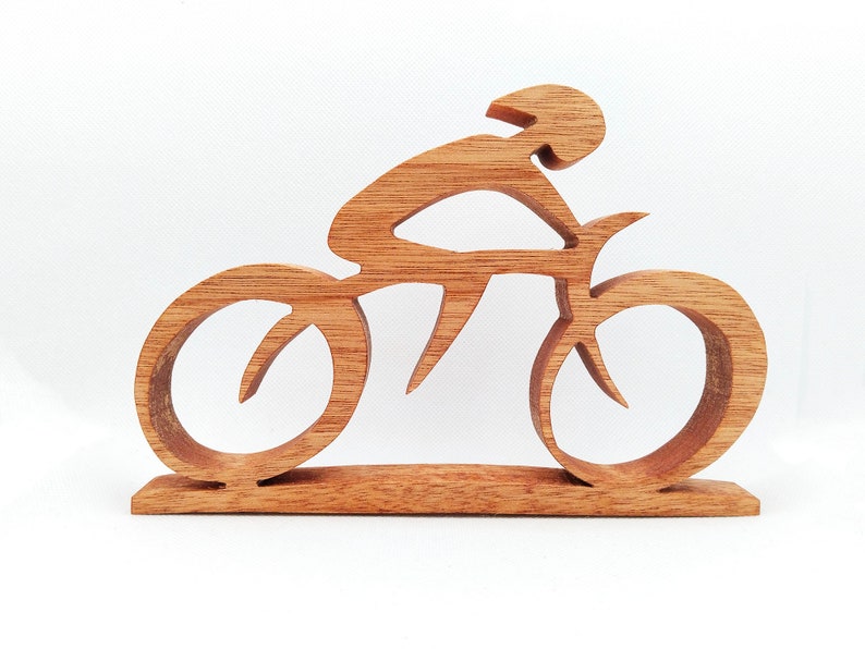 Peut inclure: Sculpture en bois repr&eacute;sentant un cycliste sur un v&eacute;lo. La sculpture est faite de bois brun clair et repr&eacute;sente un cycliste portant un casque, pench&eacute; sur le guidon. Les roues et le cadre du v&eacute;lo sont &eacute;galement en bois.