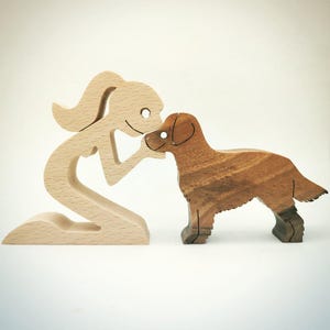 May include: Wooden figurine set depicting a person kneeling and interacting with a dog. The person is made of light-colored wood, while the dog is crafted from darker, textured wood. The dog is standing, and the person is kneeling, creating a heartwarming scene.
