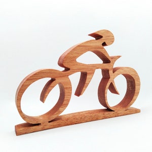 Peut inclure: Sculpture en bois repr&eacute;sentant un cycliste sur un v&eacute;lo, fabriqu&eacute;e en bois brun clair. La conception pr&eacute;sente un cycliste portant un casque sur un v&eacute;lo avec de grandes roues. La sculpture est mont&eacute;e sur une base rectangulaire, id&eacute;ale pour l'exposition.