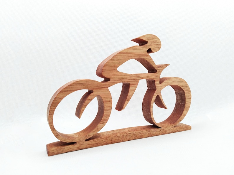 Peut inclure: Sculpture en bois repr&eacute;sentant un cycliste sur un v&eacute;lo, fabriqu&eacute;e en bois brun clair. La conception pr&eacute;sente un cycliste portant un casque sur un v&eacute;lo avec de grandes roues. La sculpture est mont&eacute;e sur une base rectangulaire, id&eacute;ale pour l'exposition.