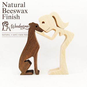 May include: A wooden figurine set featuring a dark brown dog and a light beige human figure leaning toward each other. Text on the image reads Natural Beeswax Finish, Woodensmart, and NATURAL • SAFE • NON TOXIC. The figures are smooth and stylized.