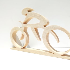 Peut inclure: Sculpture en bois repr&eacute;sentant un cycliste sur un v&eacute;lo. La sculpture est faite de bois clair et pr&eacute;sente un cycliste dans une pose a&eacute;rodynamique. Les roues et le cadre du v&eacute;lo sont &eacute;galement visibles. La sculpture est mont&eacute;e sur une base rectangulaire.