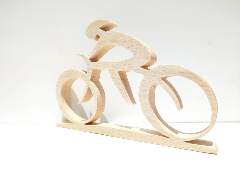 Peut inclure: Sculpture en bois repr&eacute;sentant un cycliste sur un v&eacute;lo. La sculpture est faite de bois clair et pr&eacute;sente un cycliste dans une pose a&eacute;rodynamique. Les roues et le cadre du v&eacute;lo sont &eacute;galement visibles. La sculpture est mont&eacute;e sur une base rectangulaire.