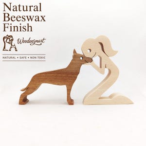 Pode incluir: Um conjunto de figuras de madeira com uma pessoa de cor clara ajoelhada e um cão de cor escura em pé. O texto diz Natural Beeswax Finish, Woodensmart e NATURAL • SAFE • NON TOXIC. As figuras são feitas de madeira lisa com acabamento natural.