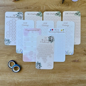 Könnte beinhalten: Eine Sammlung von Spar-Challenge-Karten mit floralen Akzenten, darunter 26-Wochen-, 5€-, 10€-, 20€-, 100€-, 250€- und 500€-Challenges. Enthält einen Stift, Washi-Tape, Büroklammern und runde Aufkleber.