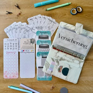 Op de afbeelding: Een marmerpatroon ringband met inlegvellen, pennen en briefpapier. Inclusief budgetbladen, spaartrackers en een 52-weken challenge kaart. Ook een blauwe markeerstift, groene pen, washitape en paperclips.