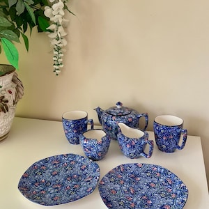 May include: A blue floral patterned tea set including a teapot, creamer, sugar bowl, two mugs, two cups, and two plates. The set features a detailed floral design in shades of blue and pink.