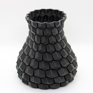 Peut inclure: Un vase en céramique noire avec un motif géométrique. Le vase est fait d'un matériau texturé et a une large ouverture en haut.