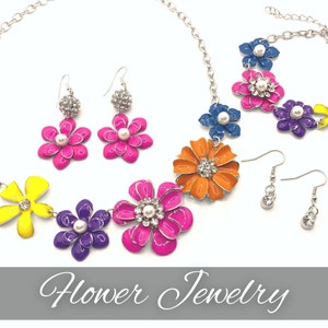 May include: A colorful flower jewelry set with a necklace, earrings, and a pendant. The necklace features a chain with five large flowers in different colors, including yellow, purple, pink, orange, and blue. The earrings are silver with a small flower design and a pearl in the center. The pendant is a single flower with a pearl in the center.