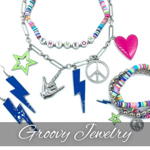 May include: A multi-piece jewelry set featuring a necklace and bracelet made of colorful clay disc beads and silver-tone chain links. Charms include a pink heart, a lime green star, a blue lightning bolt, a peace sign, and a hand gesture.