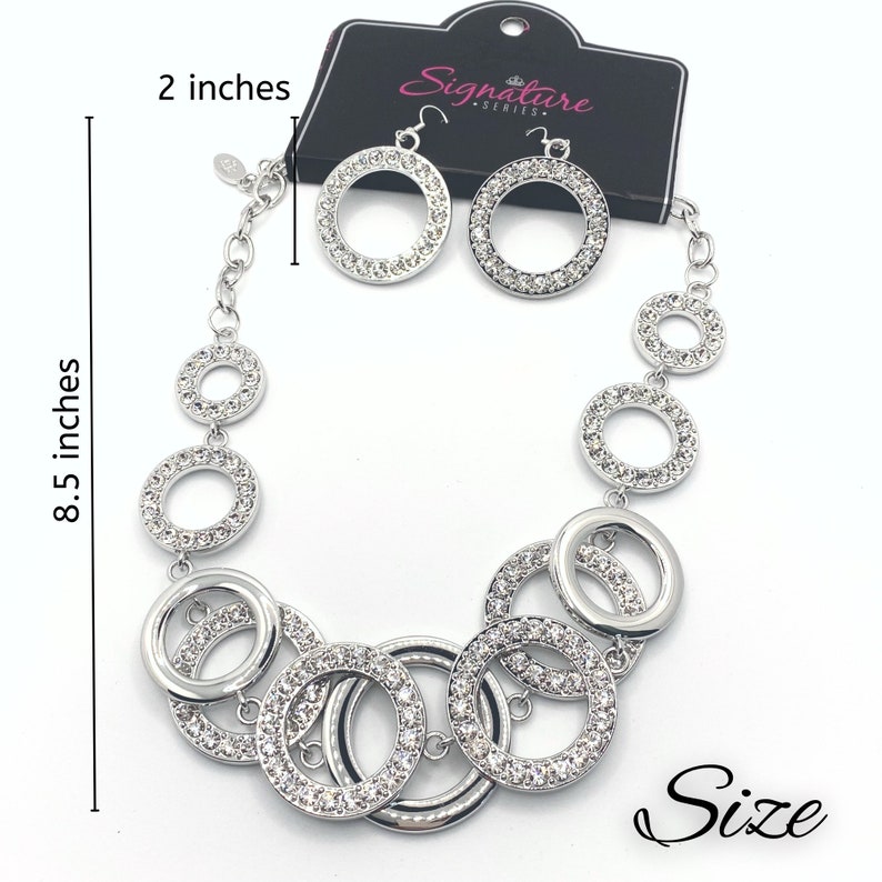 May include: A silver-toned necklace and earring set. The necklace is 8.5 inches long and features multiple open circles, some encrusted with clear crystals. The earrings are 2 inches in diameter and match the necklace design. The set is displayed on a white background.