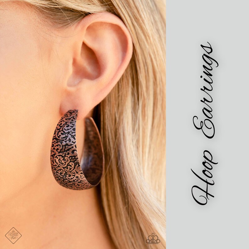 May include: Copper hoop earrings with an intricate floral pattern. The earrings are large and have a rustic look.