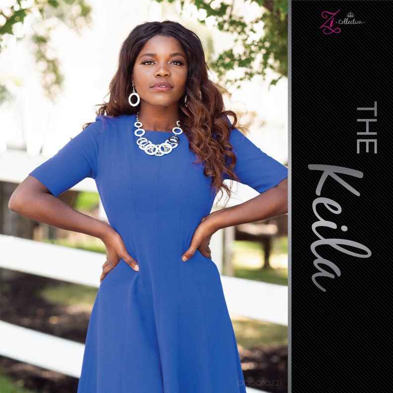 May include: A woman wearing a royal blue dress and silver-toned jewelry. The jewelry includes a statement necklace and matching earrings. The dress has short sleeves and a fitted bodice. The text "The Keila" is on the right side of the image.