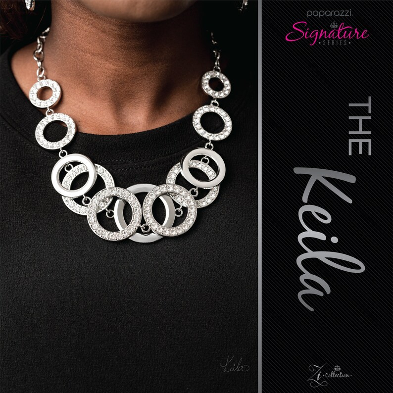 May include: A silver-toned necklace with multiple circular pendants, some encrusted with clear rhinestones. The necklace is displayed against a black background. The text "The Keila" and "Paparazzi Signature Series" are visible.