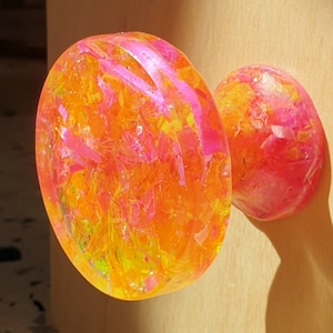 May include: A bright yellow and pink resin door knob with a swirl pattern. The knob is made of clear resin with embedded glitter and small pieces of pink and yellow.