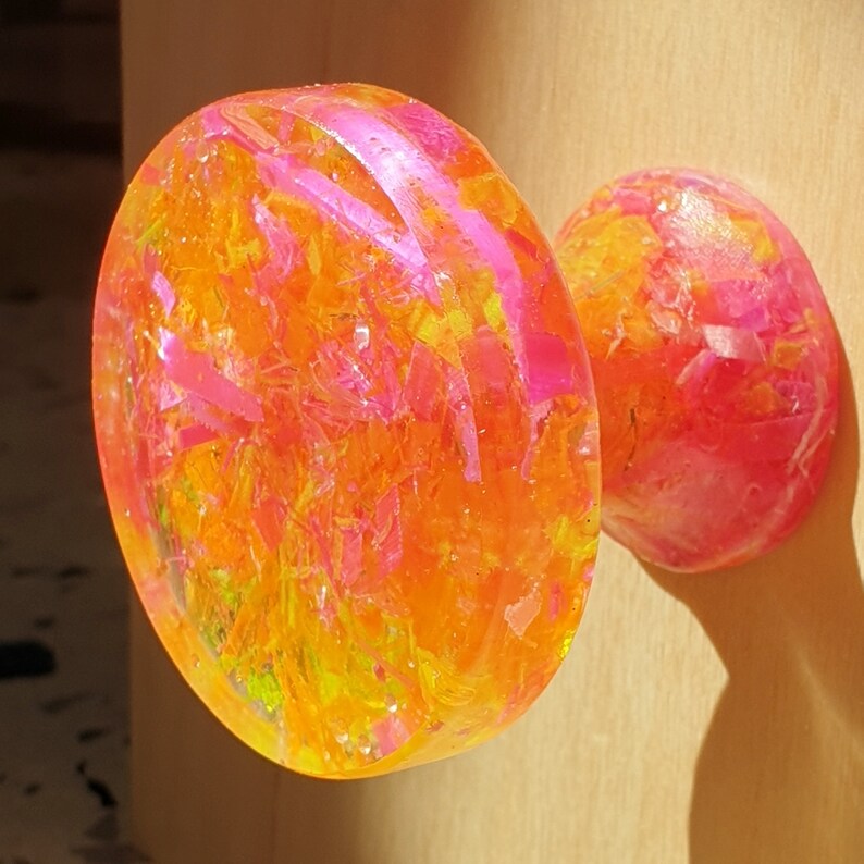 May include: A bright yellow and pink resin door knob with a swirl pattern. The knob is made of clear resin with embedded glitter and small pieces of pink and yellow.