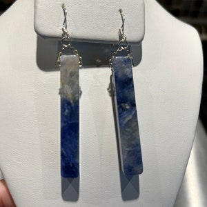 Peut inclure: Une paire de boucles d'oreilles rectangulaires avec un motif marbr&eacute; bleu et blanc. Les boucles d'oreilles sont suspendues &agrave; des crochets et des cha&icirc;nes de couleur argent&eacute;e. Les boucles d'oreilles sont expos&eacute;es sur un pr&eacute;sentoir &agrave; bijoux blanc.
