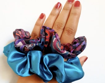 May include: Two hair scrunchies, one blue satin and one patterned with paisley designs in shades of purple, red, and black.