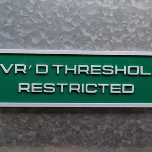 May include: A white rectangular sign with a green background and white text that reads "SVR'D THRESHOLD RESTRICTED".