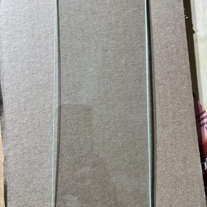 May include: A clear, rectangular glass screen protector with rounded corners. The screen protector has a thin, light blue border and is designed to fit a rectangular device. The glass is transparent and appears to be new.