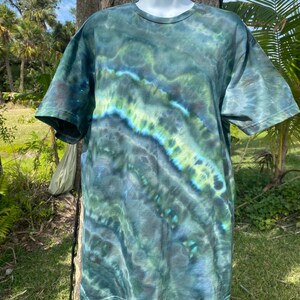 May include: A tie-dye t-shirt with a green, blue, and black swirl pattern. The shirt is made of a soft, comfortable fabric and has a crew neck.