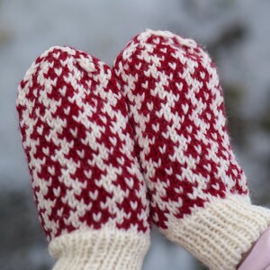 Könnte beinhalten: Ein Paar rote und weiße Strickhandschuhe mit geometrischem Muster. Die Handschuhe sind aus Wolle und haben eine weiche, warme Textur.