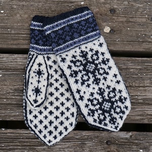 Puede incluir: Un par de guantes tejidos de color blanco y azul con un patrón de copo de nieve. Los guantes tienen un puño a rayas azul y blanco.