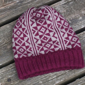 Può includere: Un cappello di lana color borgogna con un motivo geometrico beige e borgogna.