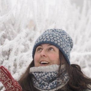 May include: A woman wearing a blue and white knitted hat and matching scarf, looking up at the sky. The background is a snowy, wintery scene.