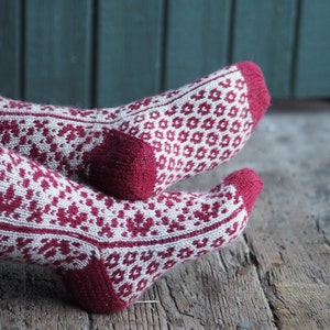 Puede incluir: Un par de calcetines de punto rojos y blancos con un patrón geométrico. Los calcetines están doblados y colocados sobre una superficie de madera.