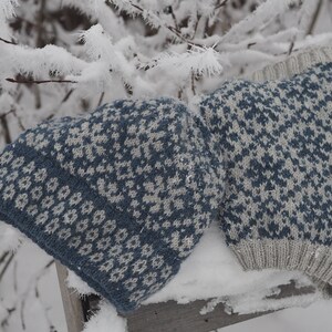 May include: Two knitted hats with a blue and white geometric pattern. The hats are lying on a snowy surface.