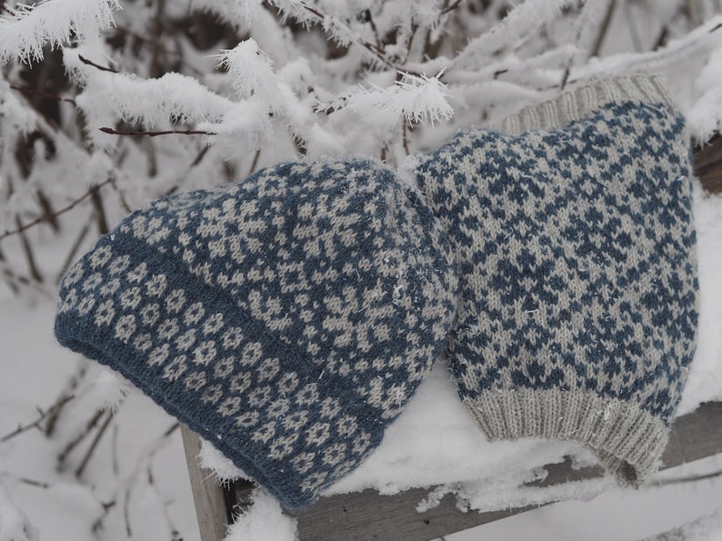 May include: Two knitted hats with a blue and white geometric pattern. The hats are lying on a snowy surface.