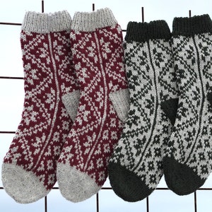 Pode incluir: Quatro pares de meias de malha com desenhos estampados. Dois pares são bordô com calcanhares, dedos e punhos cinzentos. Os outros dois pares são cinzentos com calcanhares, dedos e punhos verde escuro. As meias estão penduradas numa grelha metálica.