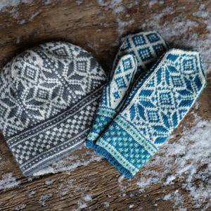K&ouml;nnte beinhalten: Eine graue und wei&szlig;e Strickm&uuml;tze und ein Paar blaue und wei&szlig;e Strickhandschuhe mit geometrischem Muster.