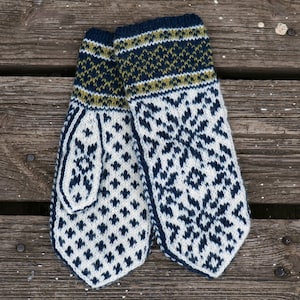 Könnte beinhalten: Ein Paar gestrickte Fäustlinge mit einem weißen, blauen und grünen Muster. Die Fäustlinge haben ein Schneeflockenmuster und eine Manschette mit einem gestreiften Muster.