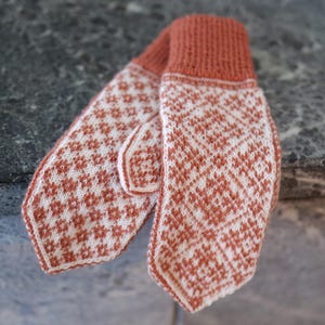 May include: A pair of knitted mittens with a white and orange geometric pattern. The mittens are made of a soft, warm yarn and are perfect for keeping your hands warm in the winter.