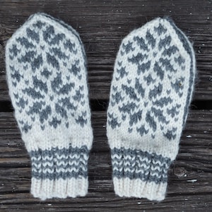 Pode incluir: Um par de luvas de malha branca e cinza com um padrão de floco de neve. As luvas têm um punho cinza.