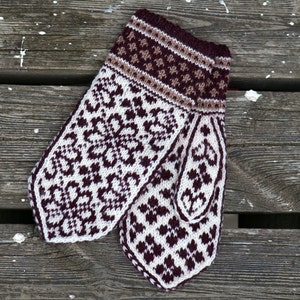Op de afbeelding: Een paar gebreide wanten met een wit en bruin geometrisch patroon. De wanten zijn gemaakt van fijn garen en hebben een zacht, comfortabel gevoel.