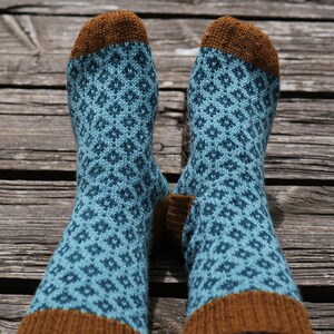 Puede incluir: Un par de calcetines de color azul y marrón con un patrón de rombos. Los calcetines son de punto y tienen un puño marrón.