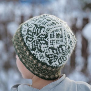 Può includere: Un cappello invernale lavorato a maglia con un motivo a fiocco di neve bianco e verde. Il cappello ha un bordo verde e un disegno bianco e verde sulla corona. Il cappello è realizzato in un materiale morbido e caldo, circa 20 cm di diametro.