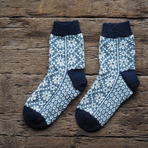 Könnte beinhalten: Ein Paar blaue und weiße gemusterte Socken mit dunkelblauem Bündchen. Die Socken sind gestrickt und haben ein Schneeflockenmuster.