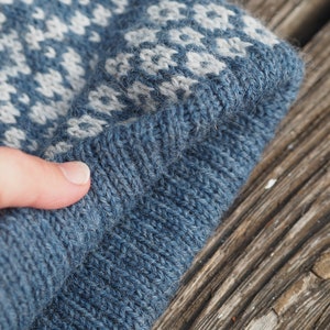 May include: A blue knitted hat with a white and blue patterned design. The hat is folded in half and the edge is visible.