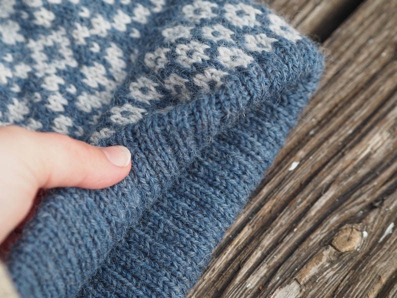 May include: A blue knitted hat with a white and blue patterned design. The hat is folded in half and the edge is visible.