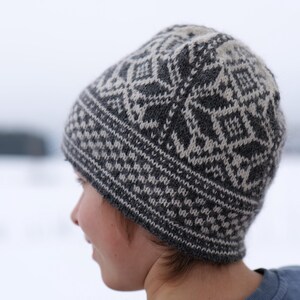 K&ouml;nnte beinhalten: Eine graue und wei&szlig;e Strickm&uuml;tze mit geometrischem Muster. Die M&uuml;tze ist aus Wolle und hat ein warmes, gem&uuml;tliches Gef&uuml;hl.
