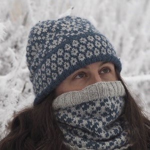 May include: A blue and white knitted hat and neck warmer with a geometric pattern. The hat is pulled down over the person's forehead and the neck warmer is pulled up to cover the person's mouth and nose.