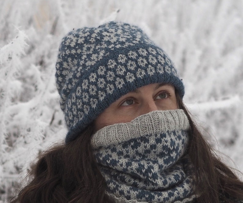 May include: A blue and white knitted hat and neck warmer with a geometric pattern. The hat is pulled down over the person's forehead and the neck warmer is pulled up to cover the person's mouth and nose.